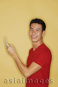 Asia Images Group - Young man holding mobile phone, looking at camera