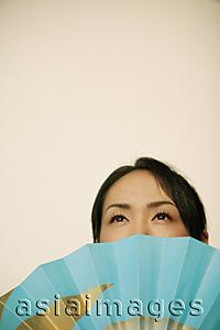 Asia Images Group - Young woman, face obscured by fan