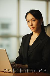 Asia Images Group - Young woman sitting at desk, using laptop, looking at camera