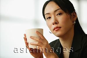 Asia Images Group - Young woman sitting at desk, holding mug