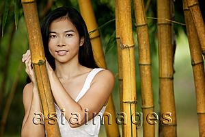 Asia Images Group - Young woman standing amongst bamboo canes, smiling