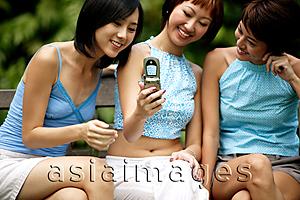 Asia Images Group - Three young women sitting side by side, using camera phone, posing