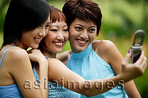 Asia Images Group - Three young women, side by side, using camera phone, posing