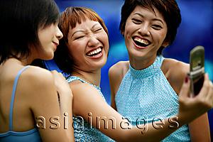 Asia Images Group - Three young women, side by side, using camera phone, posing