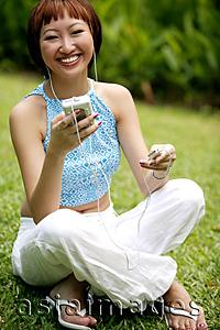 Asia Images Group - Young woman listening to personal stereo, looking at camera