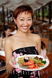 Asia Images Group - Young woman holding a plate of food, looking at camera