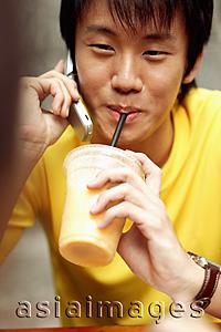 Asia Images Group - Young man on the phone, holding cup and drinking too.