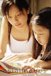 Asia Images Group - Mother and daughter, side by side, looking at magazine