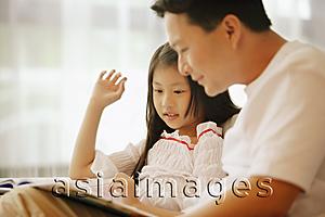 Asia Images Group - Father and daughter, sitting side by side, looking at book
