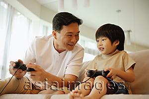Asia Images Group - Father and son sitting on sofa, playing with video game