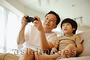 Asia Images Group - Father and son sitting on sofa, playing with video game, low angle view