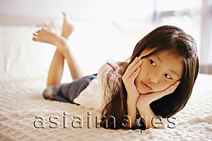 Asia Images Group - Young girl with hands on chin, lying on bed, looking away
