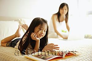 Asia Images Group - Mother using laptop, daughter flipping through book