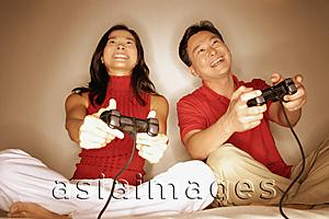 Asia Images Group - Man and woman playing with handheld video game, looking forward