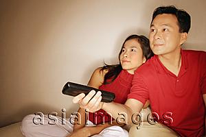 Asia Images Group - Man and woman sitting side by side, man holding remote control