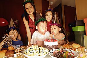 Asia Images Group - Young boy blowing out candles at a birthday party.