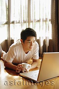 Asia Images Group - Young man using laptop, lying on floor