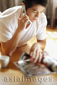 Asia Images Group - Young man reading magazine while on the phone