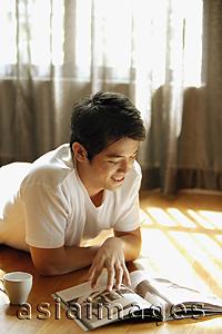 Asia Images Group - Young man reading magazine, smiling