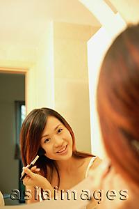 Asia Images Group - Woman putting on mascara, looking at mirror, smiling