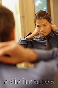 Asia Images Group - Young man adjusting tie and collar, looking in mirror