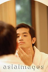 Asia Images Group - Young man  looking in mirror, touching his face