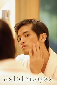 Asia Images Group - Young man touching his face, looking in mirror