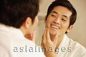 Asia Images Group - Young man touching his face, looking in mirror
