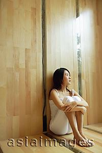 Asia Images Group - Young woman sitting, hugging knees, looking up