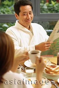 Asia Images Group - Couple at breakfast table, man holding newspaper