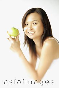Asia Images Group - Young woman lying on floor, holding apple, smiling at camera