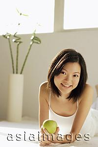 Asia Images Group - Young woman lying on front, holding green apple