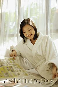 Asia Images Group - Young woman wearing robe, reading newspaper