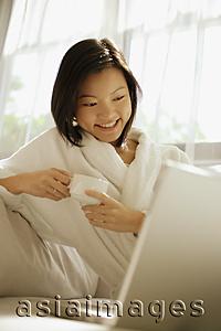 Asia Images Group - Young woman drinking coffee, laptop open in front of her