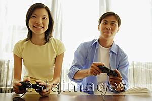 Asia Images Group - Young couple side by side, playing with handheld video game