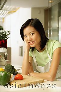 Asia Images Group - Young woman leaning on kitchen counter, smiling, looking at camera