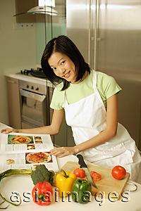 Asia Images Group - Young woman in kitchen with cookbook, looking at camera