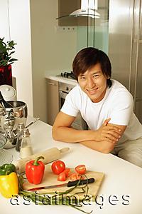 Asia Images Group - Young man leaning on kitchen counter, looking at camera