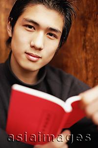 Asia Images Group - Young man holding book, looking at camera