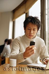 Asia Images Group - Young man sitting at table with laptop and mobile phone