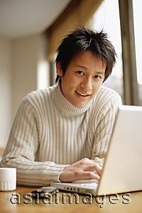 Asia Images Group - Young man sitting at table with laptop, looking at camera