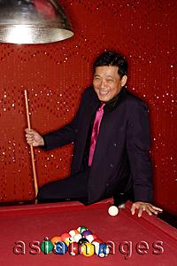 Asia Images Group - Man with pool cue leaning on table.