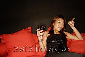 Asia Images Group - Woman holding wine glass and cigar, lying back on sofa