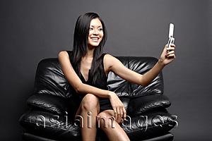 Asia Images Group -  Young woman on black chair, looking at camera phone