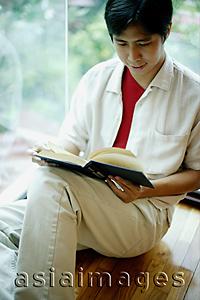 Asia Images Group - Man leaning on window, reading a book