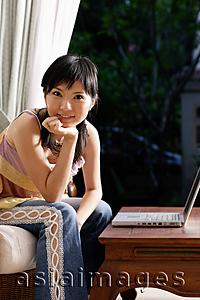 Asia Images Group - Woman with laptop, looking at camera, hand on chin