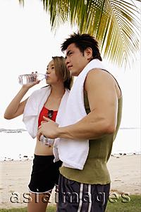 Asia Images Group - Couple standing at beach, side by side, woman drinking water