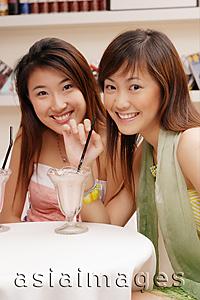 Asia Images Group -  Two young women, looking at camera, drinking milkshakes