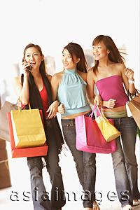 Asia Images Group - Three young women with shopping bags, walking side by side, one on the phone