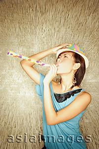 Asia Images Group - Young woman wearing hat, blowing noisemaker